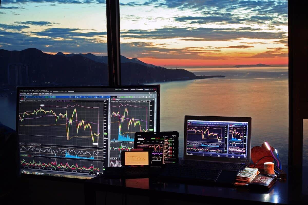 Das Bild zeigt ein Trading Setup mit mehreren mobilen Geräten mit einem Ausblick aufs Meer im Hintergrund.